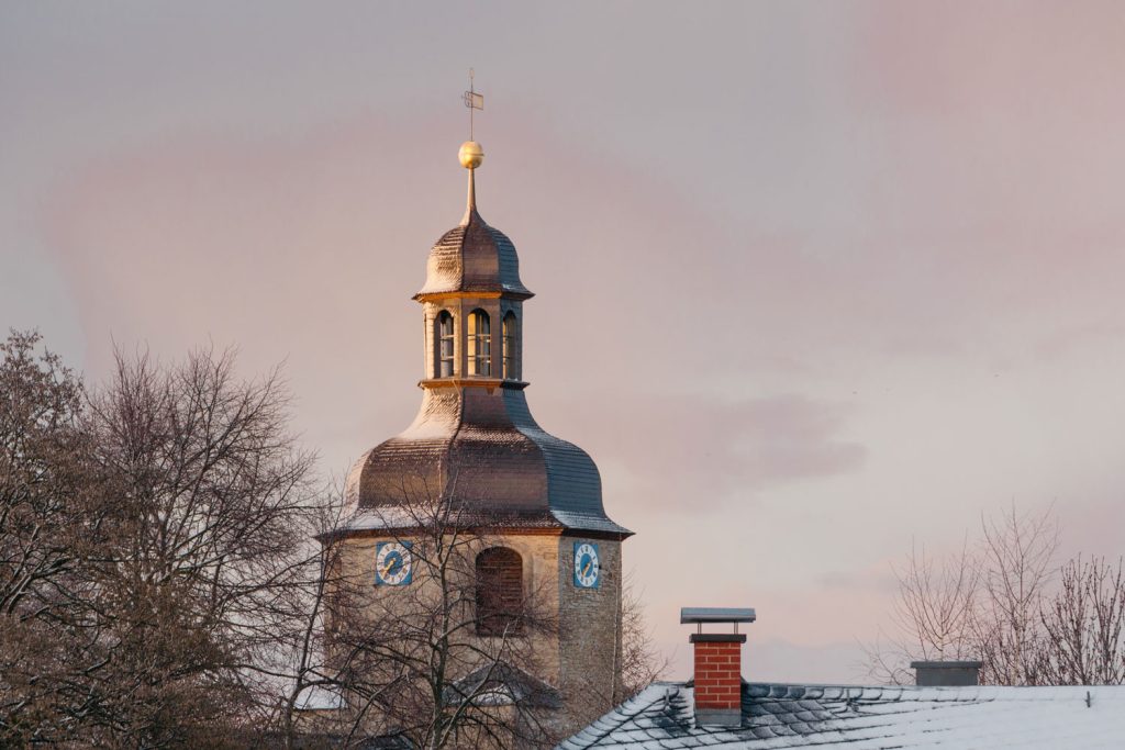 Kirchturm der Kirche St. Moritz, leicht mit Schnee bedeckt vor rosafarbenen Himmel. 