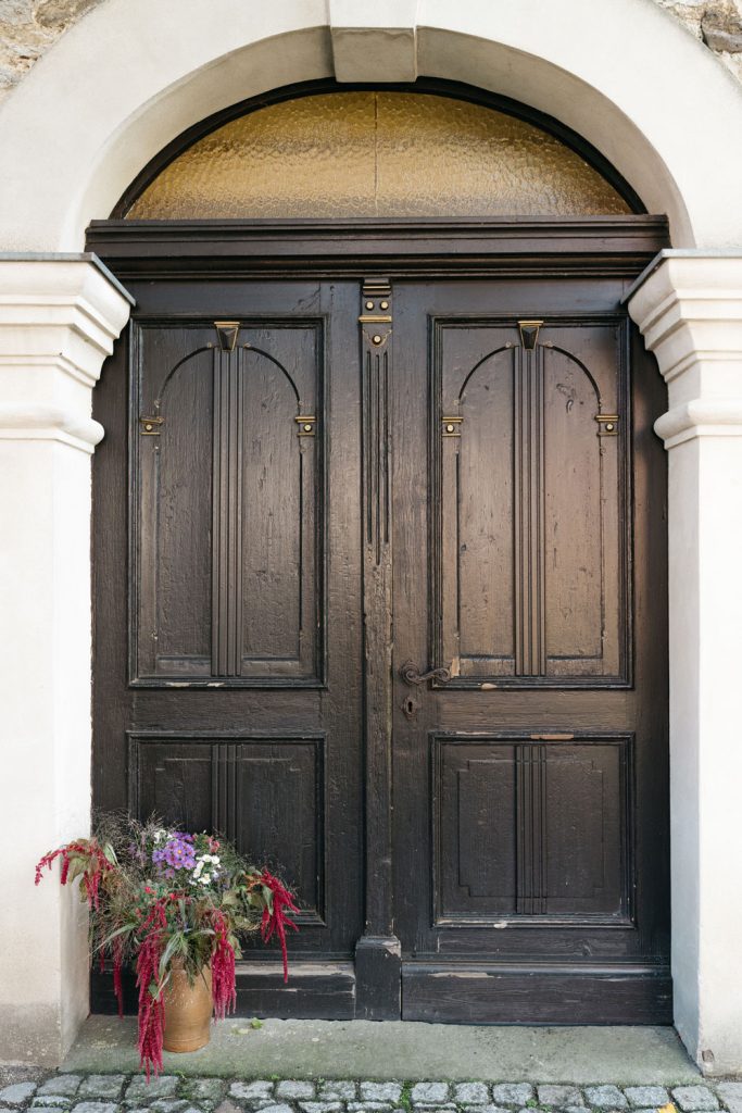 Alte zweiflüglige Holztür als Eingang zur Kirche. Davor ein Blumenstrauß in der Vase.