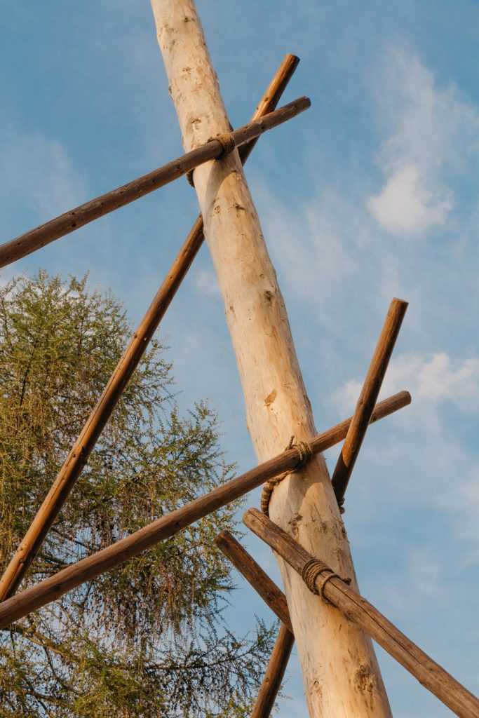 Holzpfahl des Maibaums wird durch kleine Stützpfosten aus Holz und Strick aufrecht gehalten.