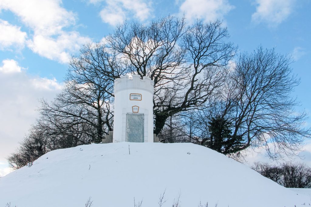 Wassertrum auf schneebedecktem Hügel mit klarem Himmel und Bäumen im Hintergrund